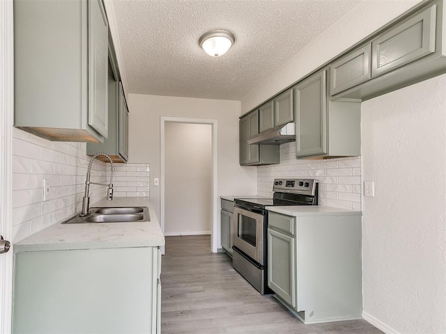 kitchen with light wood finished floors, stainless steel electric range oven, light countertops, under cabinet range hood, and a sink