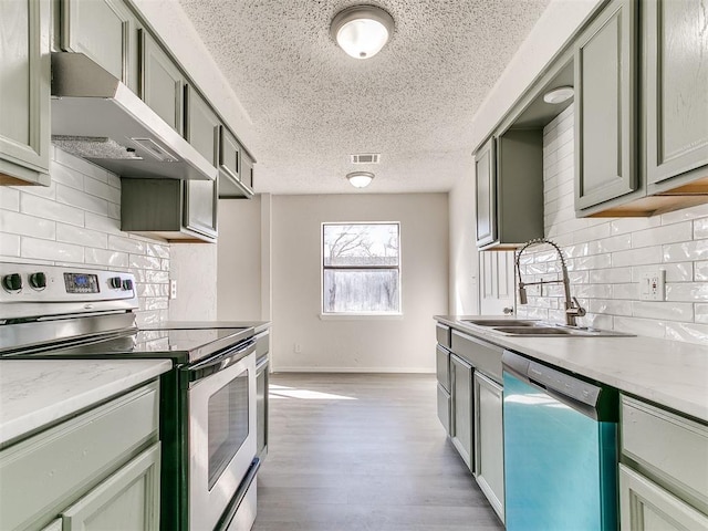 kitchen featuring under cabinet range hood, a sink, visible vents, appliances with stainless steel finishes, and light wood-type flooring