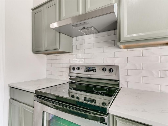 kitchen with light stone counters, exhaust hood, gray cabinets, stainless steel electric stove, and tasteful backsplash