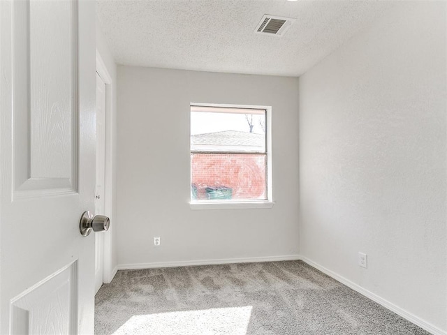 spare room featuring light carpet, baseboards, visible vents, and a textured ceiling