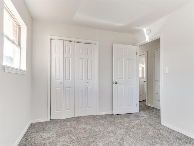 unfurnished bedroom with baseboards, a closet, and light colored carpet