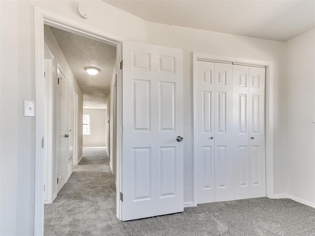 interior space featuring light carpet, a textured ceiling, baseboards, and a closet