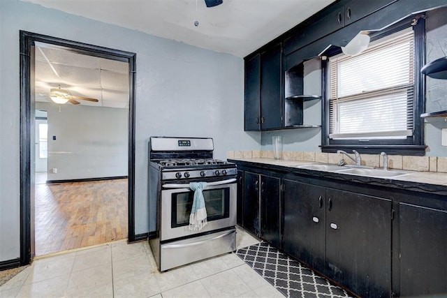 kitchen featuring dark cabinets, a sink, a ceiling fan, open shelves, and gas stove