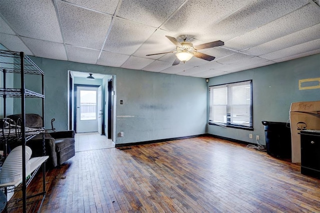 living area featuring a paneled ceiling, hardwood / wood-style flooring, ceiling fan, and baseboards