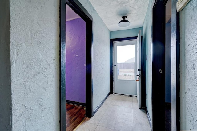 hall featuring a textured wall and baseboards