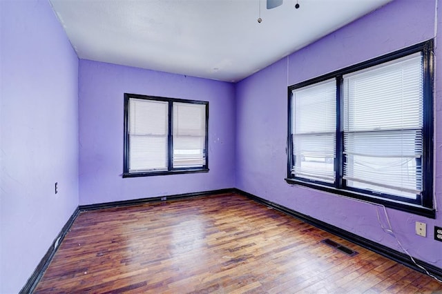 spare room featuring visible vents, plenty of natural light, baseboards, and wood finished floors