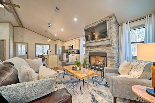 living room with vaulted ceiling with beams, a stone fireplace, wood walls, wood finished floors, and visible vents