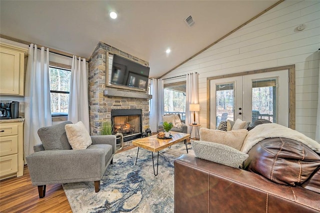 living area featuring a stone fireplace, visible vents, a healthy amount of sunlight, vaulted ceiling, and french doors