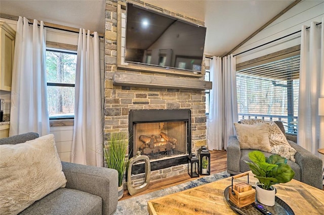 living area featuring vaulted ceiling, wood finished floors, and a stone fireplace