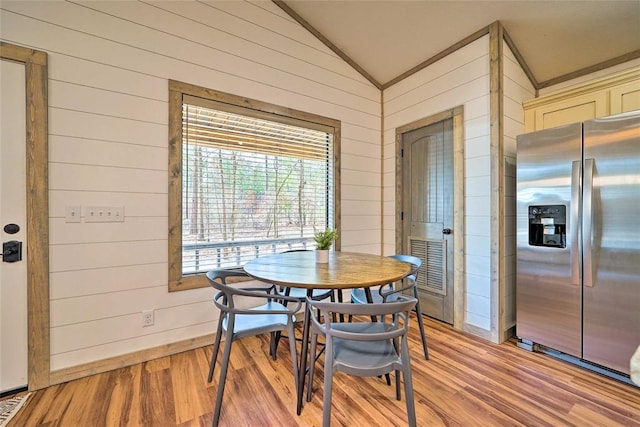 dining area with light wood-type flooring, wooden walls, baseboards, and vaulted ceiling