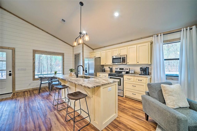 kitchen featuring a breakfast bar, appliances with stainless steel finishes, vaulted ceiling, an island with sink, and wood finished floors