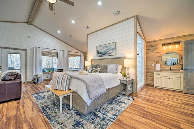 bedroom featuring visible vents, connected bathroom, light wood-style flooring, vaulted ceiling with beams, and wood walls