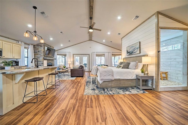 bedroom with vaulted ceiling with beams, wood walls, light wood-type flooring, and visible vents