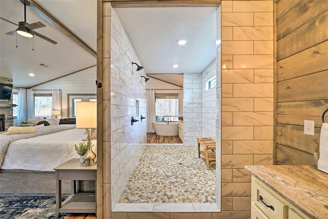 ensuite bathroom featuring a tile shower, connected bathroom, a fireplace, and a wealth of natural light