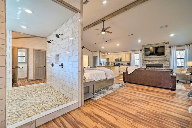 bedroom with vaulted ceiling with beams, a fireplace, visible vents, light wood-style flooring, and freestanding refrigerator