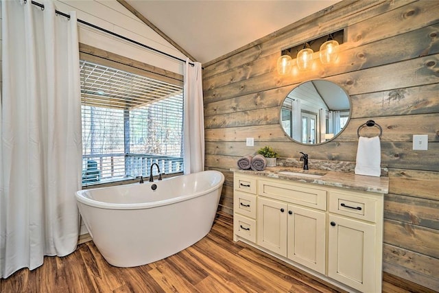 full bath featuring lofted ceiling, wood finished floors, a freestanding bath, vanity, and wood walls