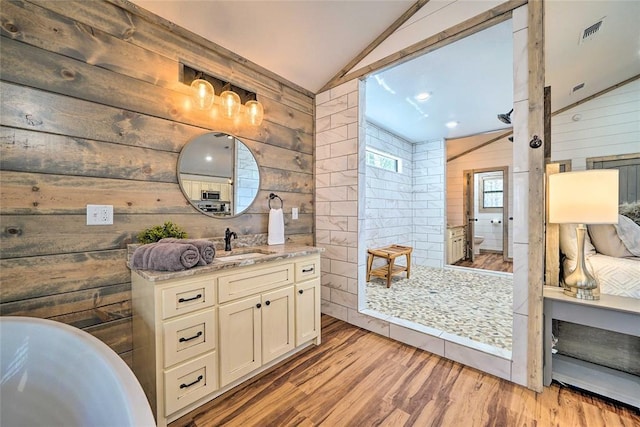 bathroom with a tile shower, wooden walls, vaulted ceiling, and wood finished floors