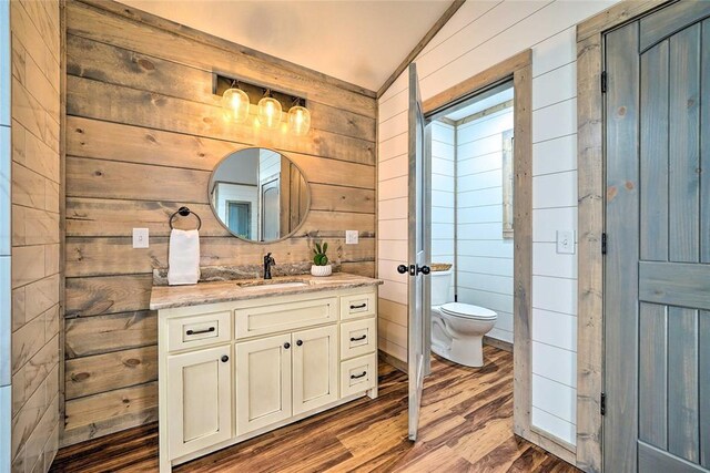 bathroom featuring toilet, wooden walls, wood finished floors, and vanity