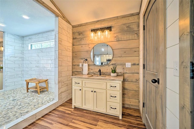 bathroom featuring wood walls, walk in shower, wood finished floors, and vanity