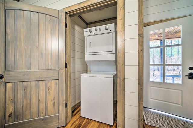 clothes washing area with stacked washer / drying machine, laundry area, wood walls, and wood finished floors