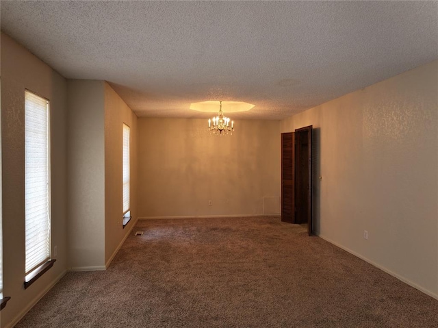 unfurnished room featuring a textured ceiling, baseboards, carpet flooring, and an inviting chandelier