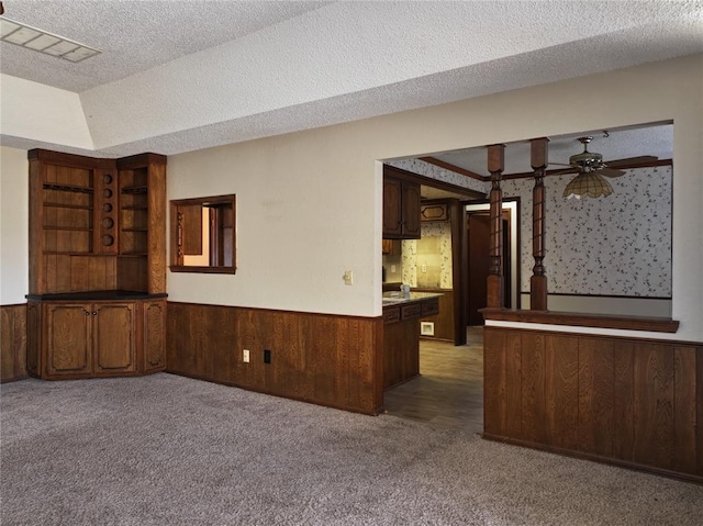 interior space with a textured ceiling, wooden walls, a wainscoted wall, visible vents, and dark colored carpet