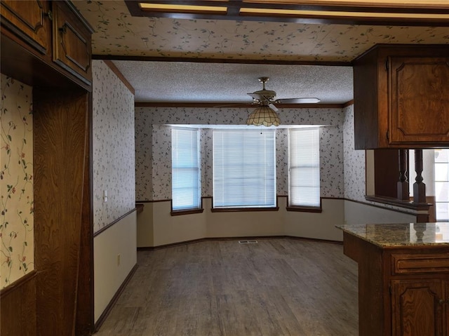 kitchen with light stone countertops, crown molding, a textured ceiling, and wallpapered walls