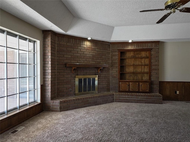 unfurnished living room with built in features, carpet floors, visible vents, wooden walls, and a textured ceiling