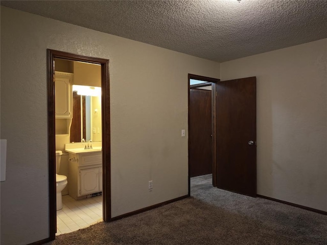 unfurnished bedroom with a textured wall, light carpet, a sink, a textured ceiling, and ensuite bath