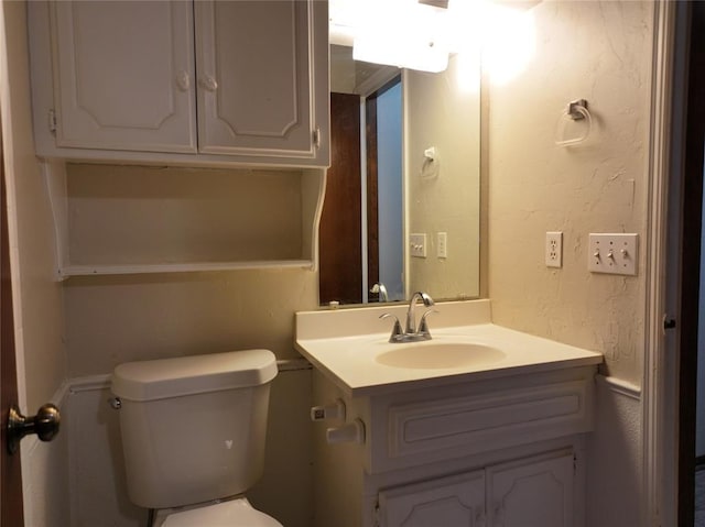 half bathroom featuring toilet, a textured wall, and vanity