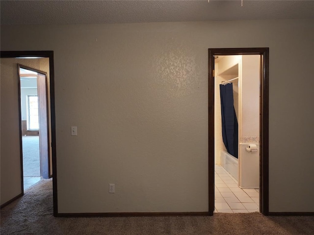 unfurnished room with light carpet, light tile patterned floors, baseboards, a textured wall, and a textured ceiling