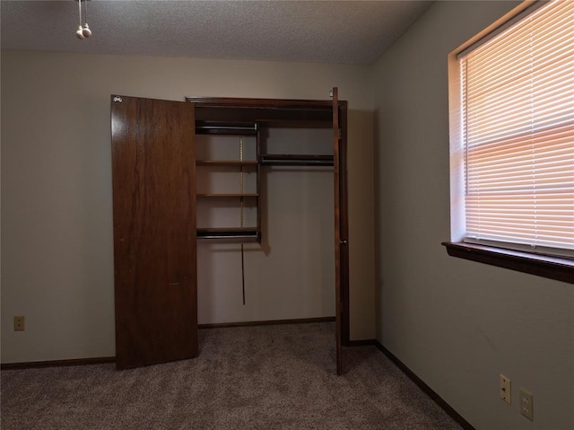 unfurnished bedroom featuring a textured ceiling, a closet, baseboards, and carpet flooring