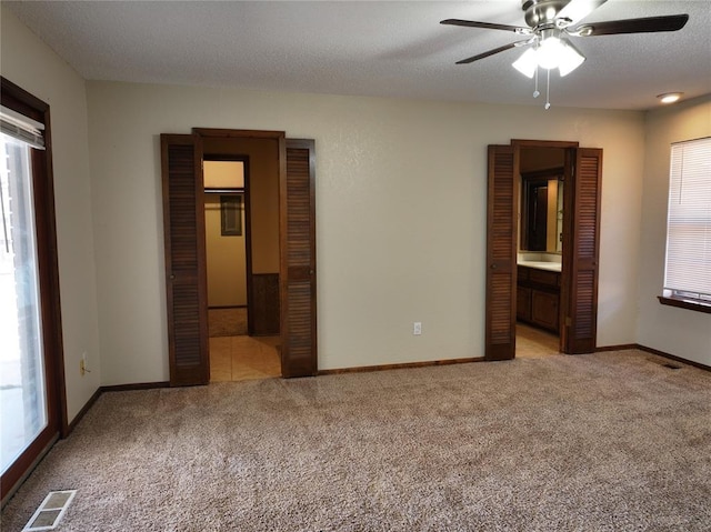 unfurnished bedroom featuring a textured ceiling, baseboards, visible vents, and light colored carpet