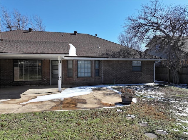 rear view of property featuring a shingled roof, brick siding, and a patio