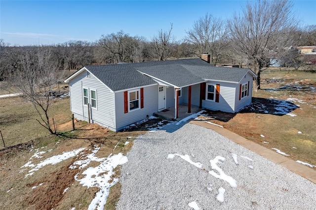 single story home featuring a shingled roof, a chimney, and gravel driveway