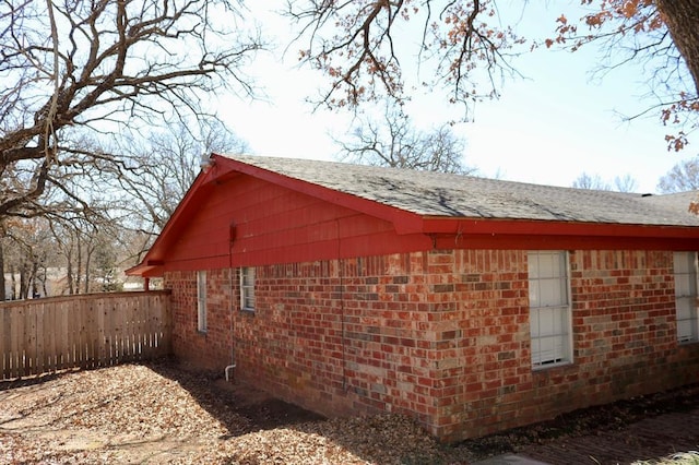 view of home's exterior featuring brick siding, roof with shingles, and fence