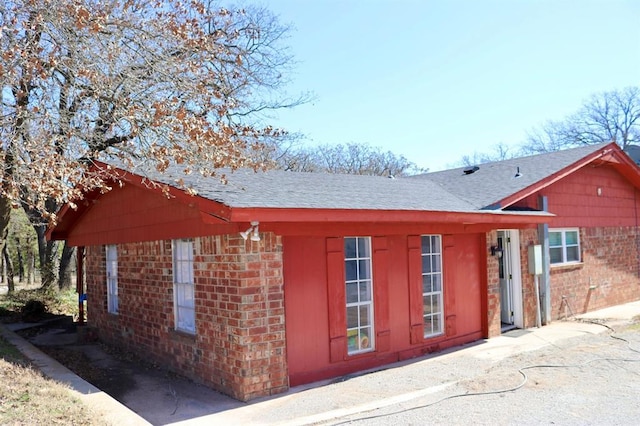 view of side of home with brick siding and roof with shingles