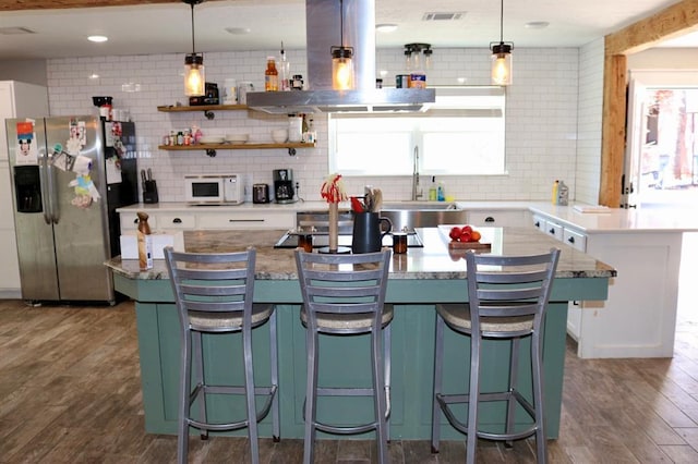 kitchen with white microwave, a sink, island exhaust hood, stainless steel refrigerator with ice dispenser, and dark wood-style flooring