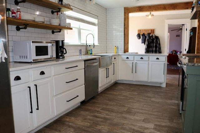 kitchen with a sink, a peninsula, white microwave, dishwasher, and dark wood-style flooring