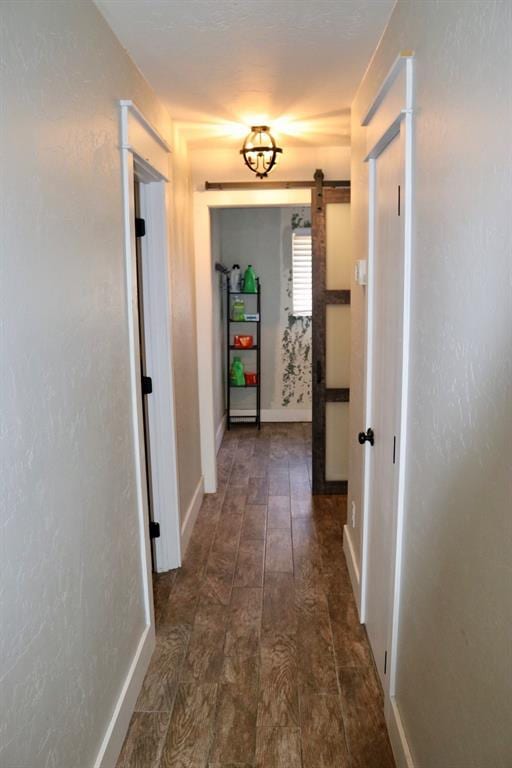 hall featuring a barn door, baseboards, and dark wood-style flooring