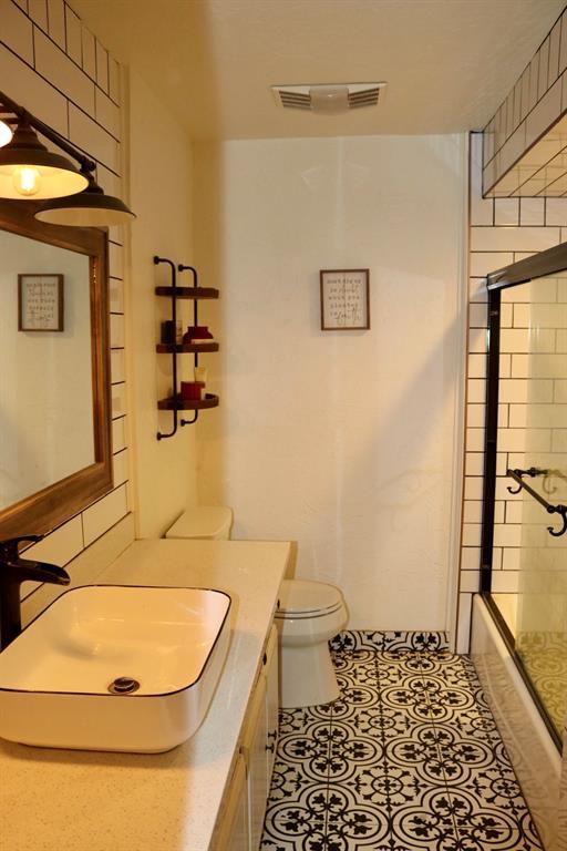 bathroom featuring vanity, visible vents, bath / shower combo with glass door, tile patterned floors, and toilet