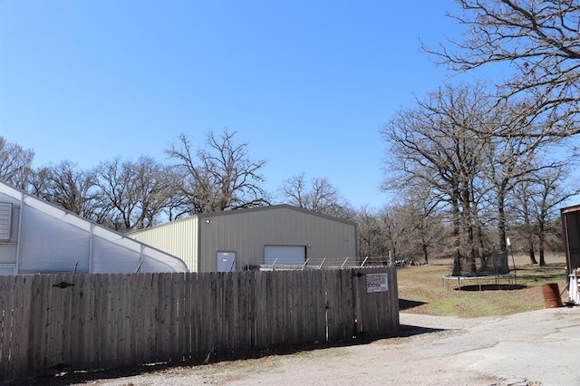 view of side of home featuring an outdoor structure, a trampoline, and fence