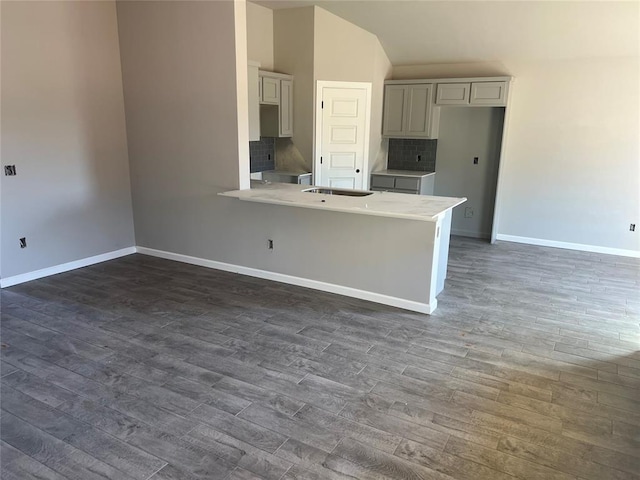 kitchen featuring decorative backsplash, lofted ceiling, dark wood-type flooring, and baseboards