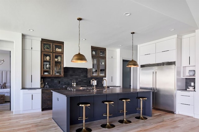 kitchen with stainless steel built in refrigerator, dark countertops, modern cabinets, and glass insert cabinets