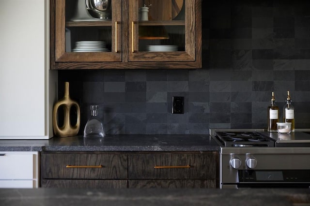 kitchen featuring dark countertops, dark brown cabinetry, glass insert cabinets, and decorative backsplash