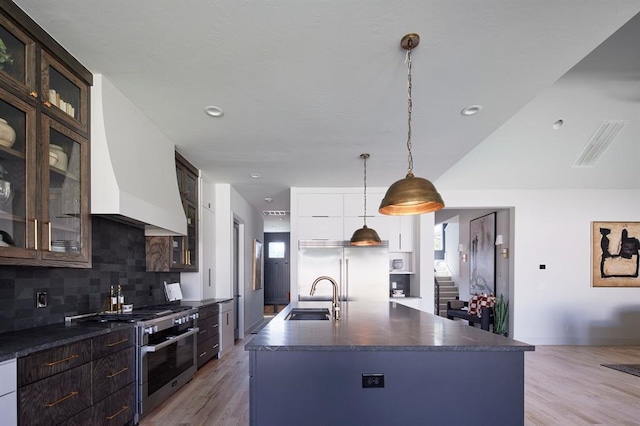 kitchen with premium appliances, dark countertops, a sink, and glass insert cabinets