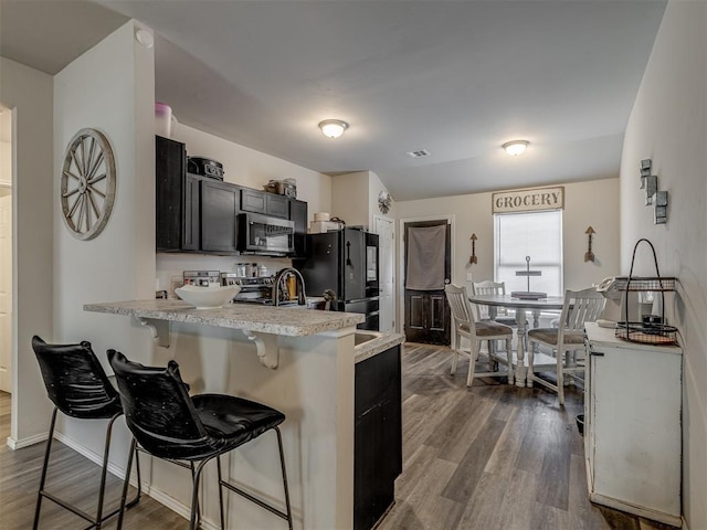 kitchen with dark cabinets, stainless steel appliances, a breakfast bar, a peninsula, and dark wood-style floors