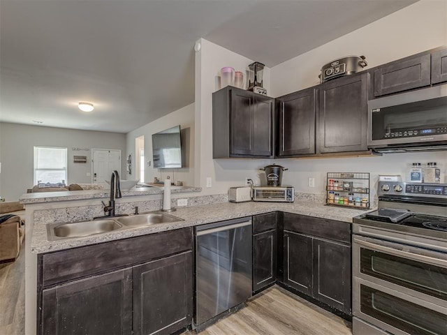 kitchen featuring appliances with stainless steel finishes, open floor plan, a peninsula, light countertops, and a sink