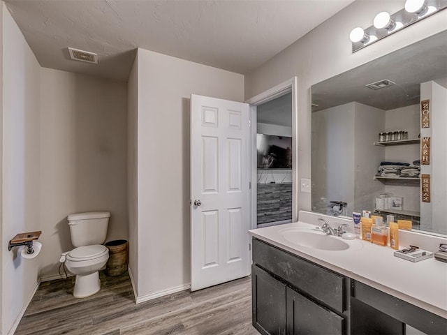 bathroom featuring toilet, visible vents, wood finished floors, and vanity