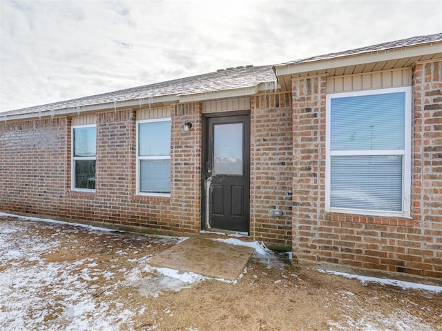 snow covered property entrance with brick siding